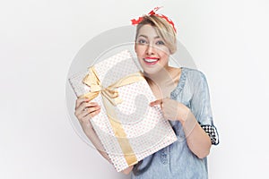 Charming smiling satisfied woman standing pointing at gift box, present for holiday.