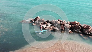 Charming sportive boy on surfboard. Young man surfing. Aerial view of sandy beach with blue clear water. Attractive boy surfing on