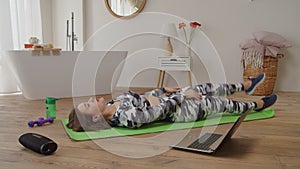 Charming sporty fitness woman practicing reclining hamstring stretch in domestic room