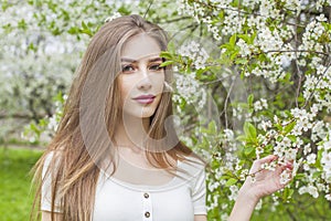 Charming spring woman fashion beauty portrait. Young model with make-up and long hair in blossom garden