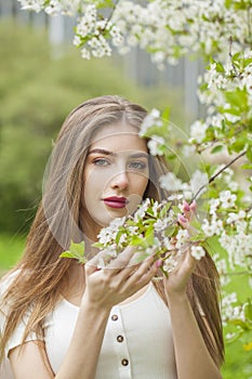Charming spring woman fashion beauty portrait. Young model with make-up and long hair in blossom garden