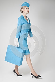 Charming Stewardess In Blue Uniform And Suitcase On Gray