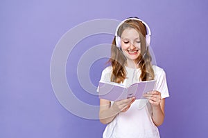 Charming student girl listening to music through headphones holds an open