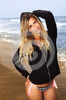 Charming and sweet young blonde girl at the sea standing with black sweatshirt.