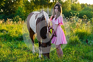 Charming teenager girl in pink dress with horse in the field