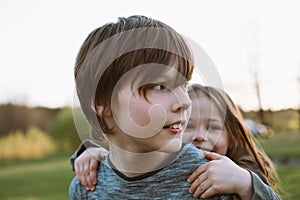 Charming teenager looking away while carrying smiling sister on back, siblings enjoying walk in village together.