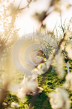 Charming tender loving couple walking in a spring blossoming garden at sunrise. Man hugs and holds his woman in arms