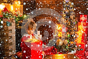 Charming toddler Santa boy looking at magic gift box with garland lights at winter Christmas background. Holidays and