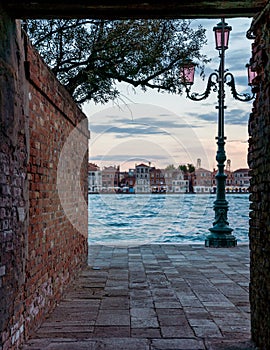 Charming view of the lagoon in Venice, Italy framed by a brick wall and a street light.