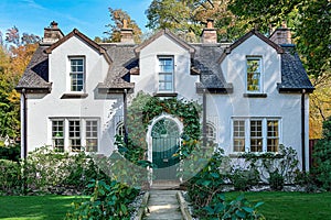 A charming white cottage house with contrasting black trim and a beautiful arched green door. Surrounded by a lush garden and