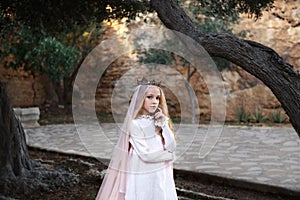 Charming white witch foreteller stands in a mysterious magical forest in a wedding dress with a veil and crown