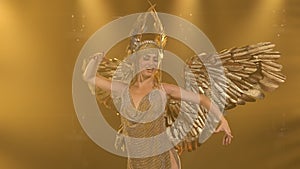 A charming woman actress in the image of the Greek goddess Artemis with golden wings sings and dances on stage