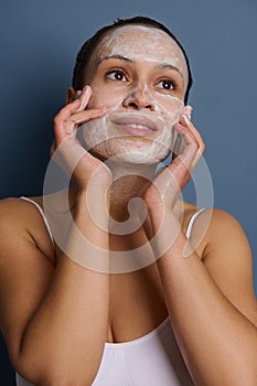 Charming woman applying foam cleansing cosmetic product on her face, doing massage movements, removing make-up and refreshing her