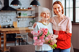 Charming woman being hugged by attractive red-haired young-adult daughter.