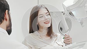 Charming woman checking her teeth in the mirror at dental clinic