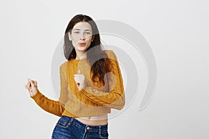 charming woman dancing with raised hands, smiling seductively and gazing at camera while being over gray background