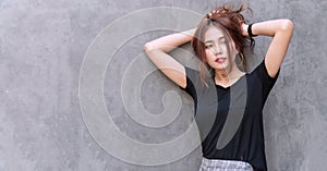 Charming woman feeling relax holding her thick hair on head over gray wall background. Cheerful girl tying her long brown