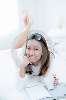 Charming woman lying on bed reading a book and holding coffee cup