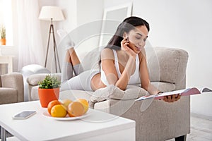 Charming woman lying on couch and reading magazine