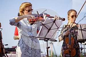 Charming woman playing violin in orchestra at outdoor concert