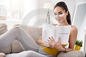 Charming woman posing with psychology book on couch