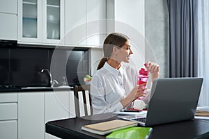 Charming woman sitting at with laptop and drinking water