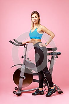 Charming woman with slim body shape posing near exercise bike and looking at camera.