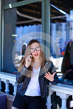 Charming woman wearing glasses and speaking by smartphone at street cafe.