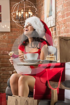 Charming woman wearing Santa Claus hat opening Christmas gift