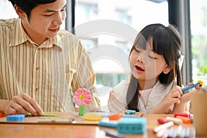 Charming young Asian girl enjoys playing play dough, moulding colorful clay with her older brother