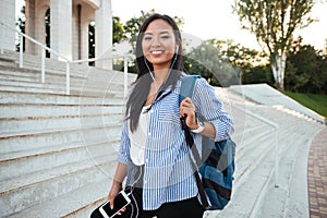 Charming young asian woman with backpack listening to music while going up stairs