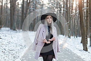 Charming young blond woman in an elegant black hat in a pink stylish coat in a black trendy dress