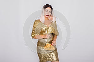 Charming young blonde haired woman wearing elegant gold evening dress and holding gold color clutch in her hands