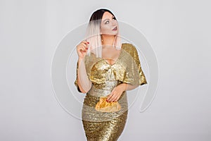 Charming young blonde haired woman wearing elegant gold evening dress and holding gold color clutch in her hands