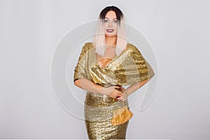 Charming young blonde haired woman wearing elegant gold evening dress and holding gold color clutch in her hands