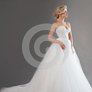 Charming young bride in luxurious wedding dress. Pretty girl in white. Emotions of happiness, gray background