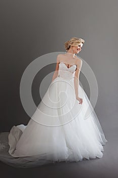 Charming young bride in luxurious wedding dress. Pretty girl in white. Emotions of happiness, gray background