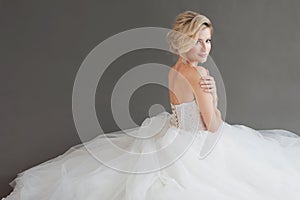 Charming young bride in luxurious wedding dress. Pretty girl in white. Gray background. Back