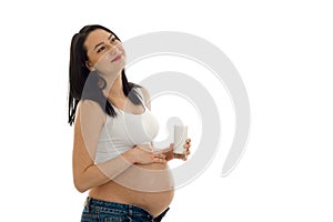 Charming young brunette pregnant girl with glasses of milk and hand on her belly posing isolated on white background