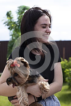 Charming young brunette woman in a black T-shirt and denim shorts with a cute dog Yorkshire terrier in her arms