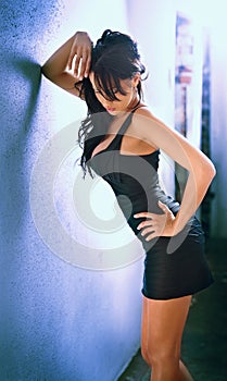 Charming young brunette woman in black tight fit dress posing against a wall