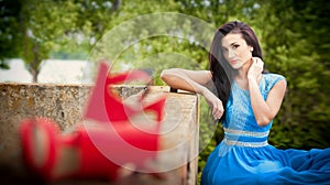 Charming young brunette woman in bright blue dress with red shoes in foreground. gorgeous fashionable woman, outdoor shot