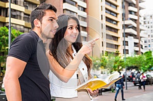 Charming young couple standing outside in urban environment, holding open book and pointing finger, urban tourist