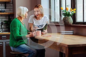 Charming young fair-haired woman discussing with short-haired pensioner Bible book