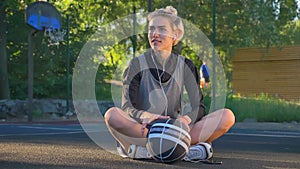 Charming young female basketball player standing up from ground and going away, holding ball, basketball court in open