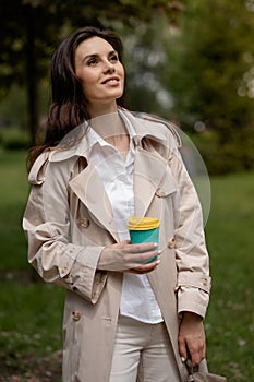 A charming young girl relaxes in a spring park outdoors with a cup of coffee after study or work. A smiling positive