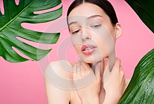 A charming young girl in tropical leaves on a pink background