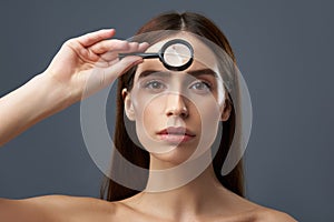 Charming young lady examining skin with magnifying glass