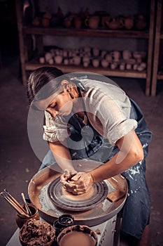 Charming young lady is working on pottery wheel. Craft manufacture.