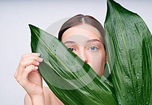 The charming young model covers part of her face with green tropical leaves